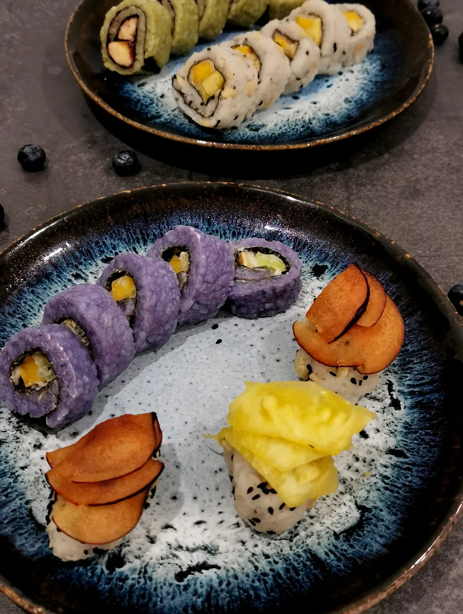 Bunte Sushirollen und Früchte auf Tellern.