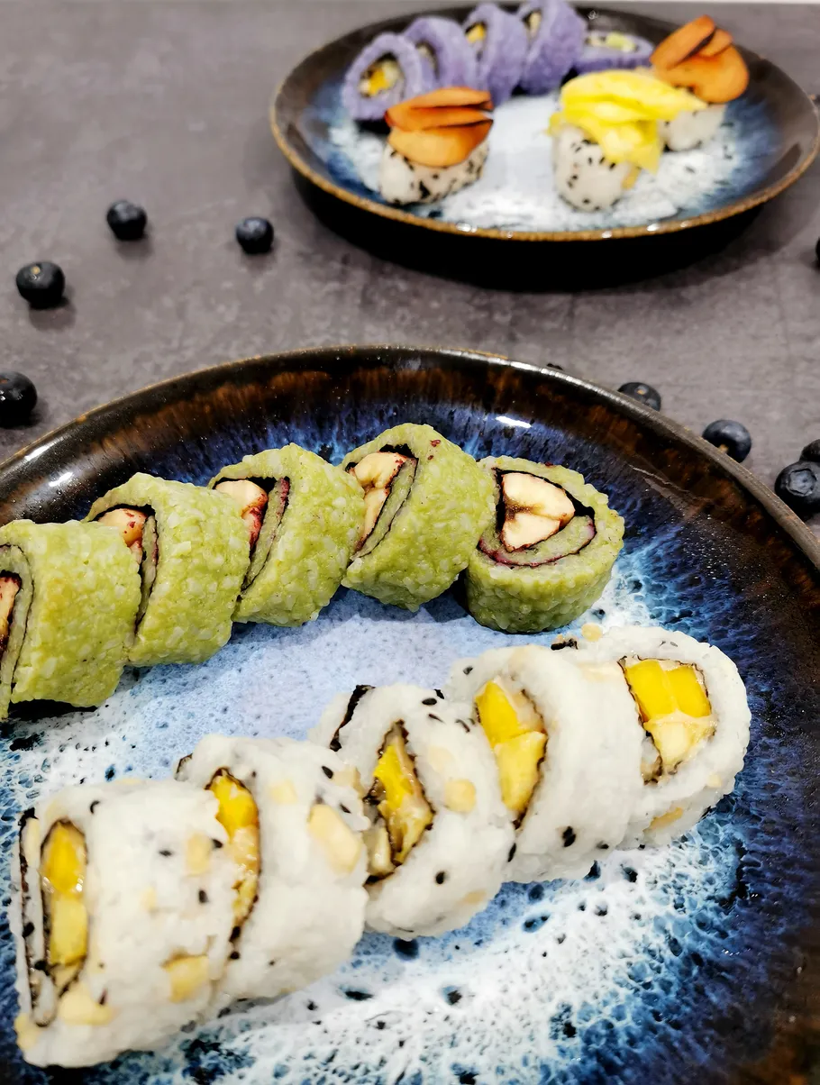 Bunte Sushirollen auf Keramiktellern, Blaubeeren in der Nähe.