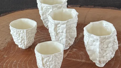 Five textured ceramic cups on wooden surface.