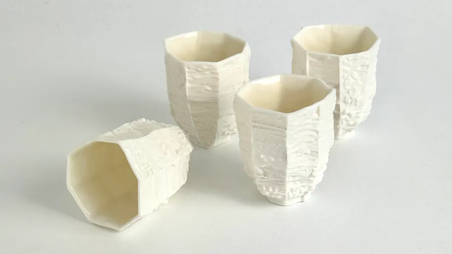 Four textured white ceramic cups on table.