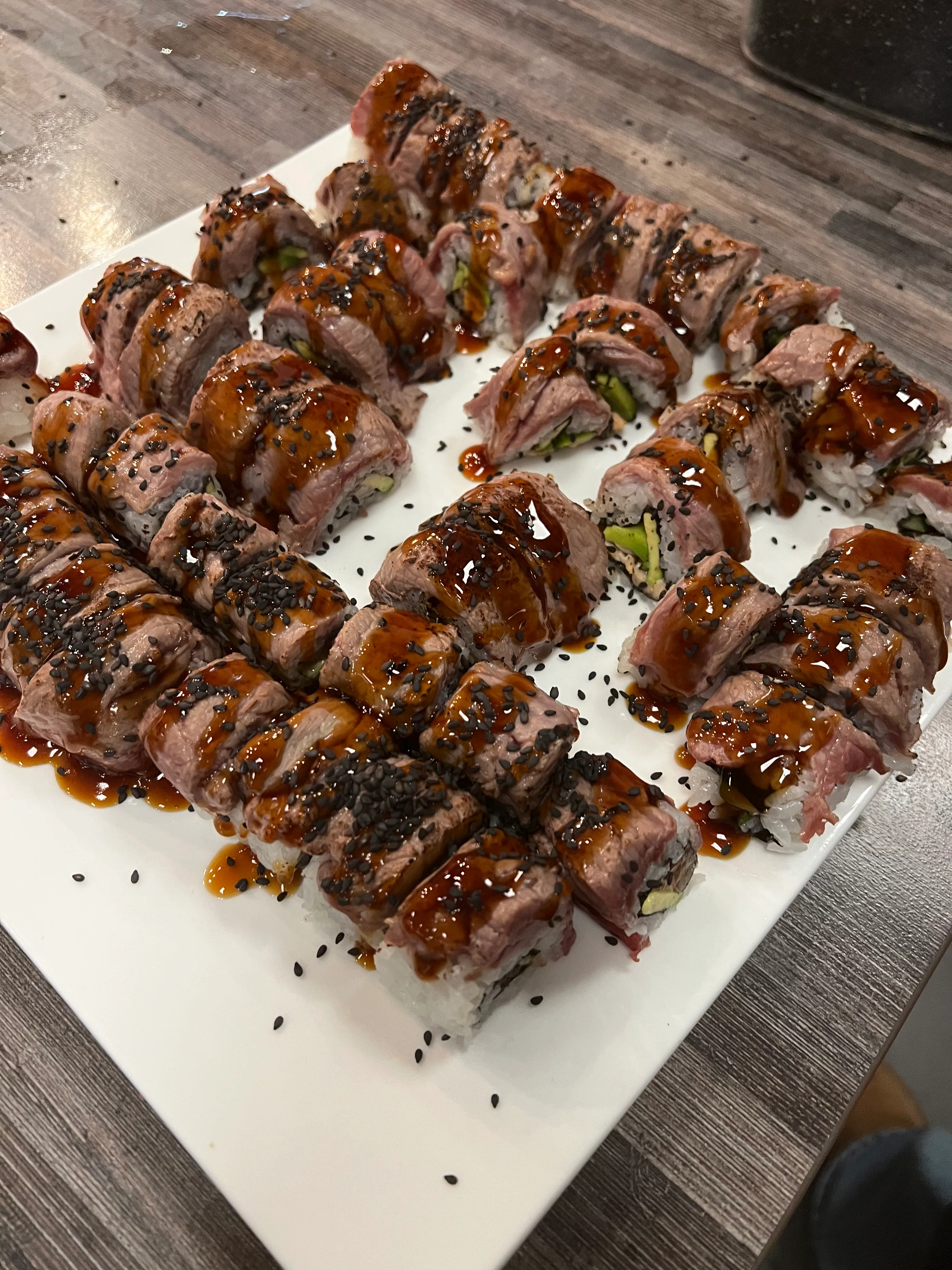 Beef-wrapped sushi rolls with sauce on platter.