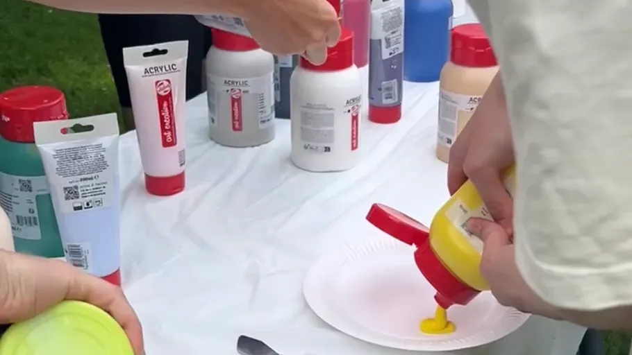 Person squeezing yellow paint onto white plate.