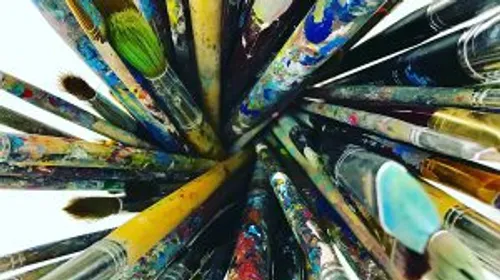 Paintbrushes clustered, covered in colorful paint.