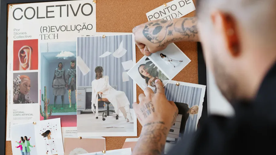 Tattooed person arranging photos on corkboard.
