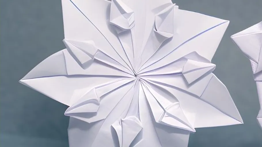 Komplexes weißes Papierorigami vor grauem Hintergrund.