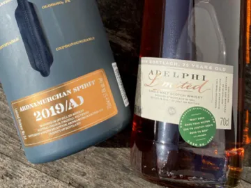 Two whiskey bottles stand on a wooden surface.