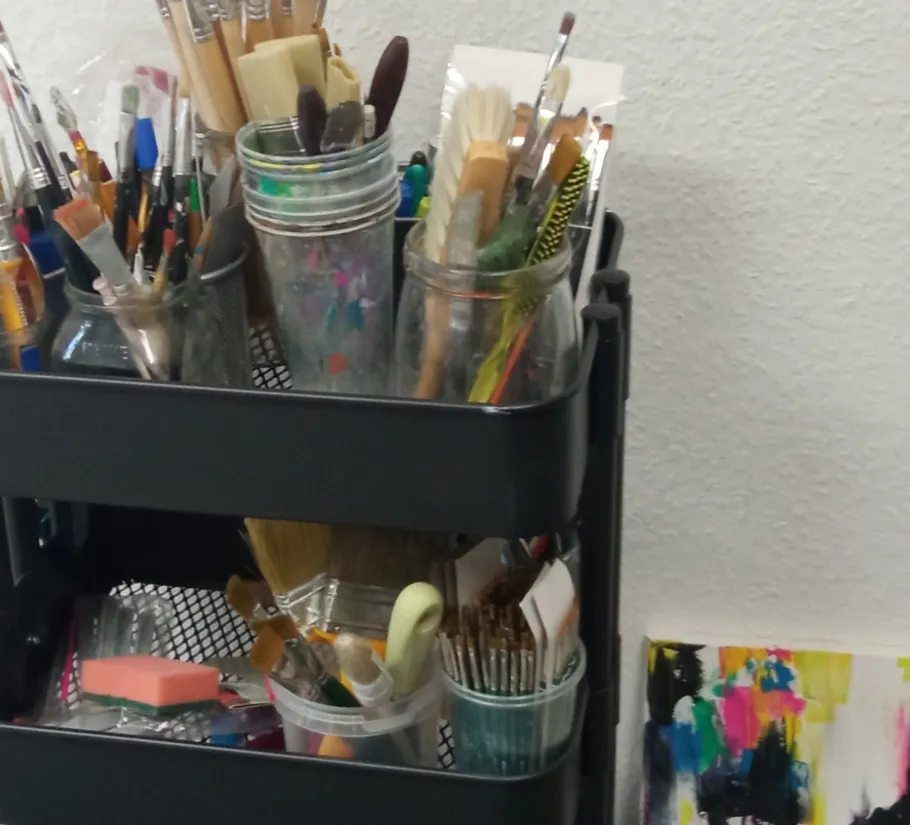 Art supplies on shelf beside abstract painting.