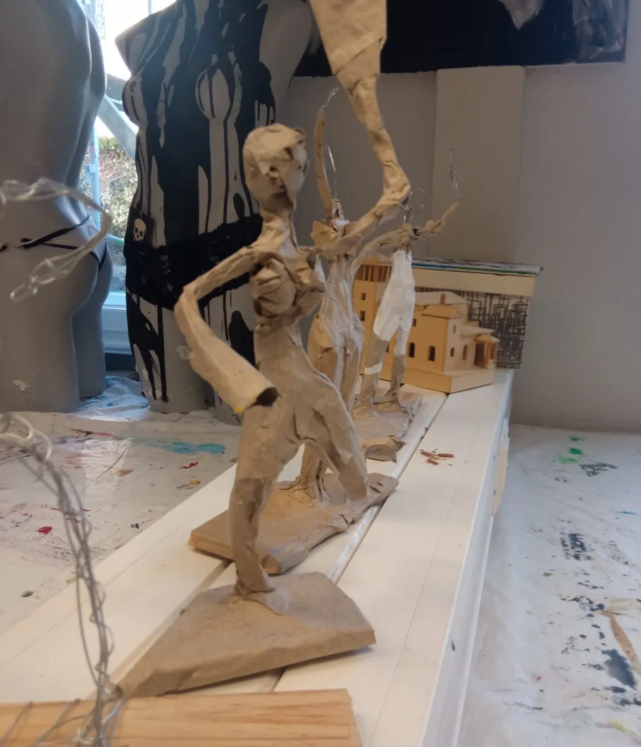 Papierskulpturen halten Fahnen auf überladenem Tisch.