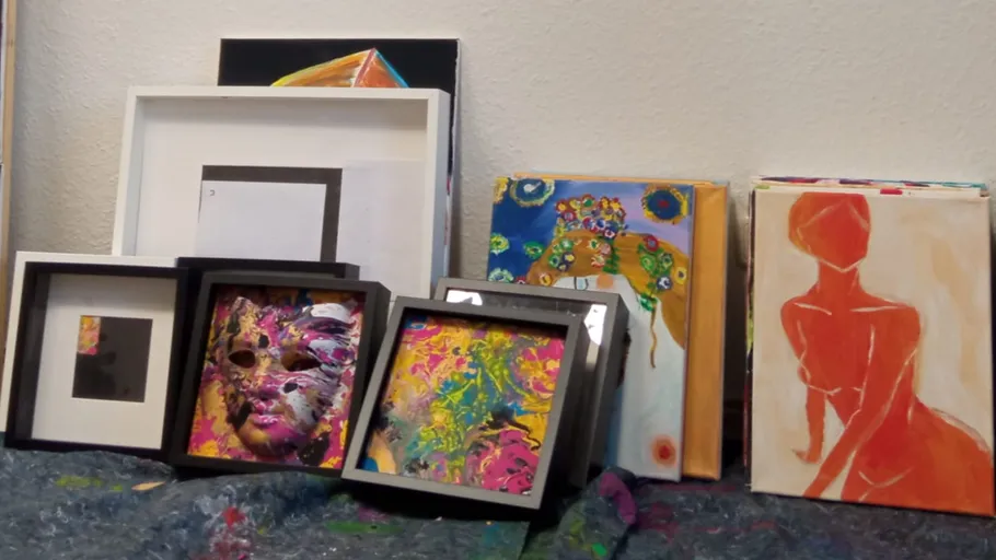 Gerahmte Kunstwerke auf Boden gegen Wand gestapelt.