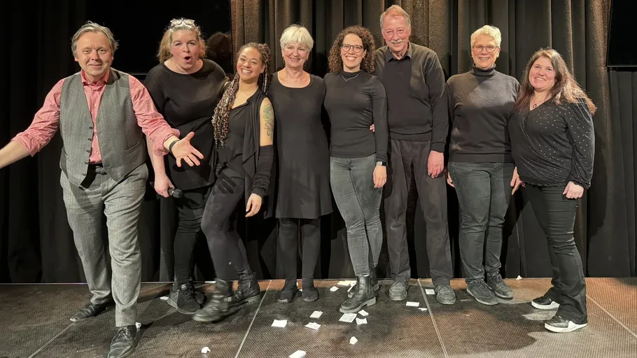 Gruppe von acht Personen auf Bühne lächelnd.