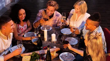 Gruppe stößt mit Weingläsern am Tisch an.