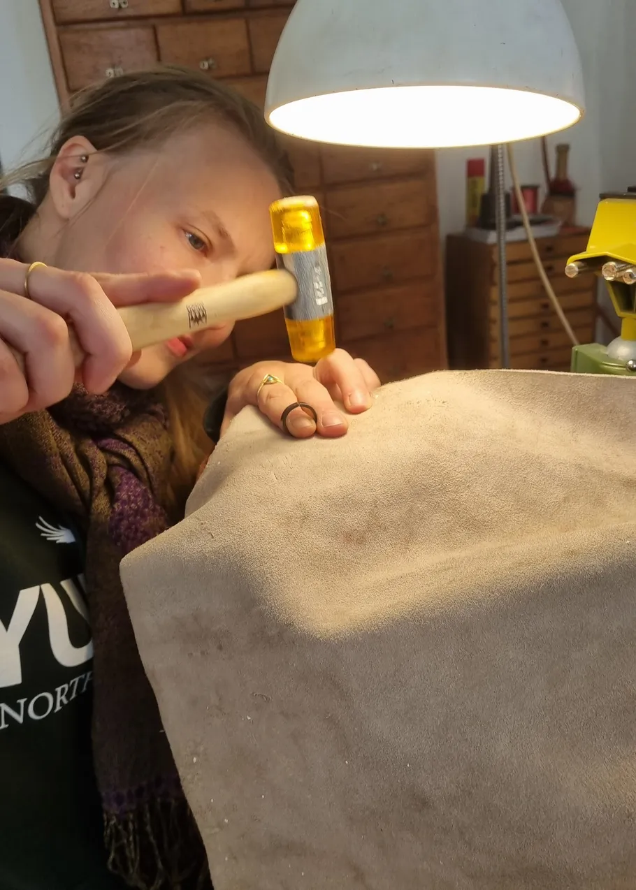 Person uses hammer on fabric under lamp.