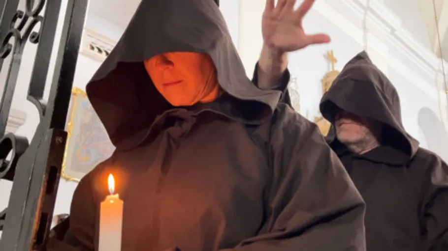 Hooded figures holding candle inside a building.