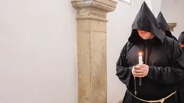 Monks holding candles walking in a corridor.