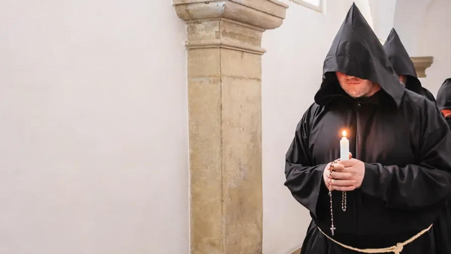 Monks holding candles walking in a corridor.