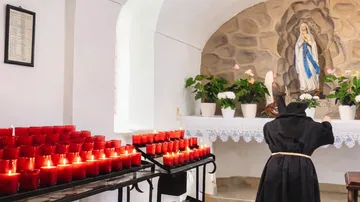 Nuns lighting candles in chapel with statue.