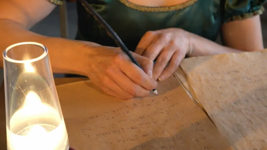 Hand schreibt mit Feder bei Kerzenlicht.