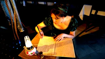 Frau schreibt in Notizbuch am Tisch mit Lampe.