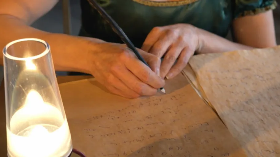 Person writing with quill by candlelight.