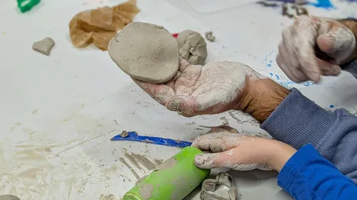 Hands molding clay on messy table.