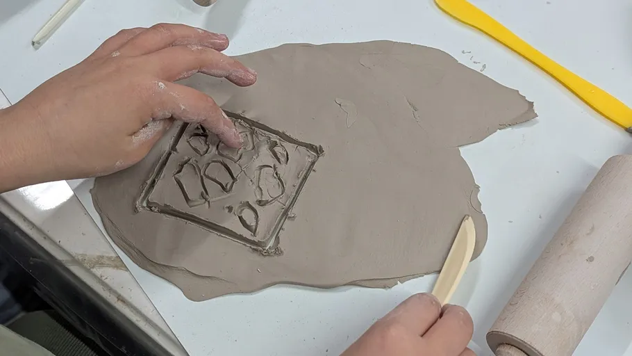 Hands shaping clay slab on table.