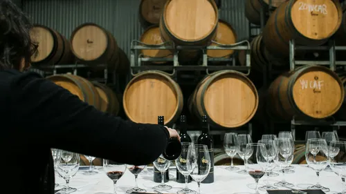 Person pouring wine in a cellar with barrels.