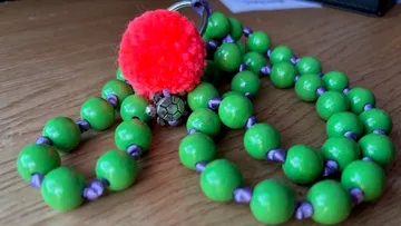 Grüne Perlen mit rotem Pompon auf Tisch.