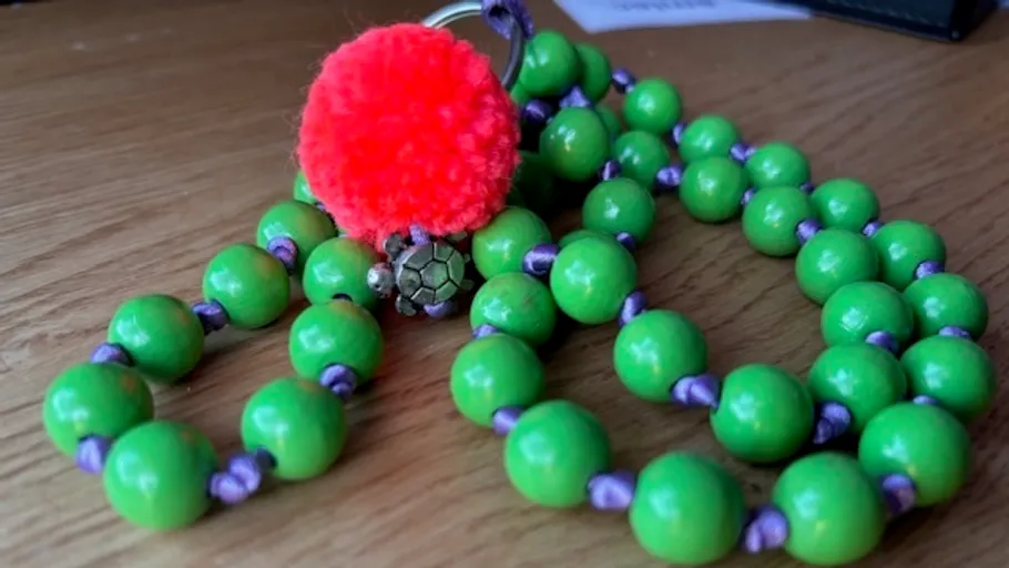 Grüne Perlen mit rotem Pompon auf Tisch.