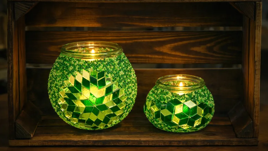 Two green mosaic candle holders glowing on shelf.