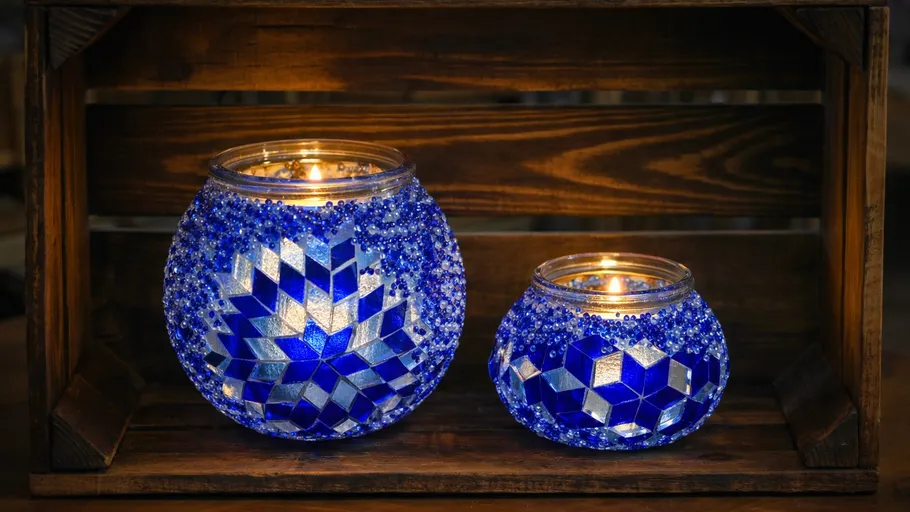 Two mosaic candle holders with lit candles indoors.