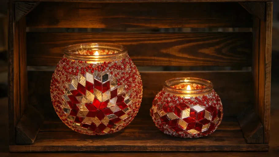Two mosaic candle holders glowing on wooden shelf.