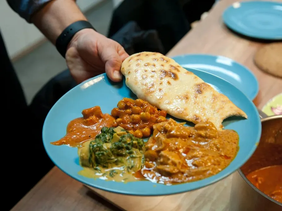 A plate of various curries and flatbread is held.
