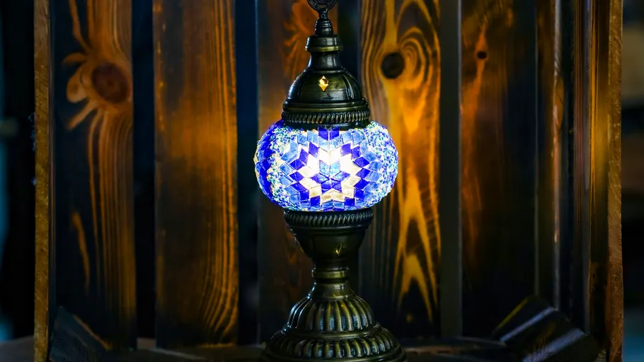 Blaue Mosaiklampe leuchtet vor Holzwand.