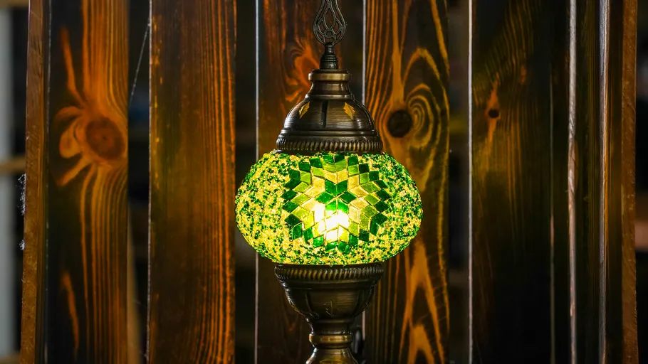 Green mosaic lamp glowing against wooden wall.