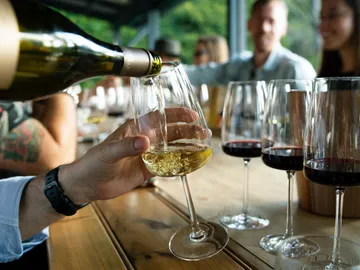 Ein Glas Wein wird eingegossen, umgeben von Freunden.