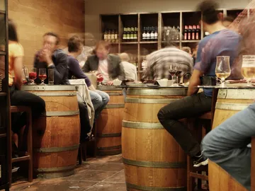 Holzfässer, Gäste sitzen und trinken in einem geselligen Restaurant.