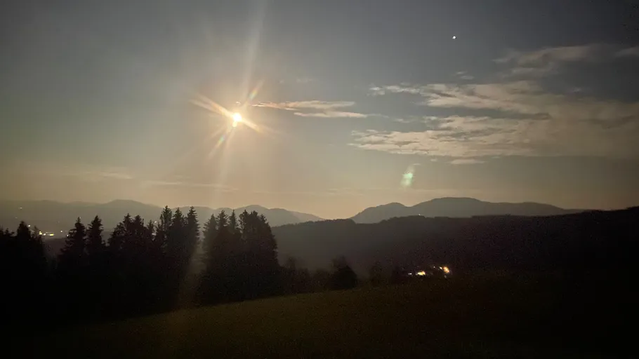 Moon shining over forested mountains at night.