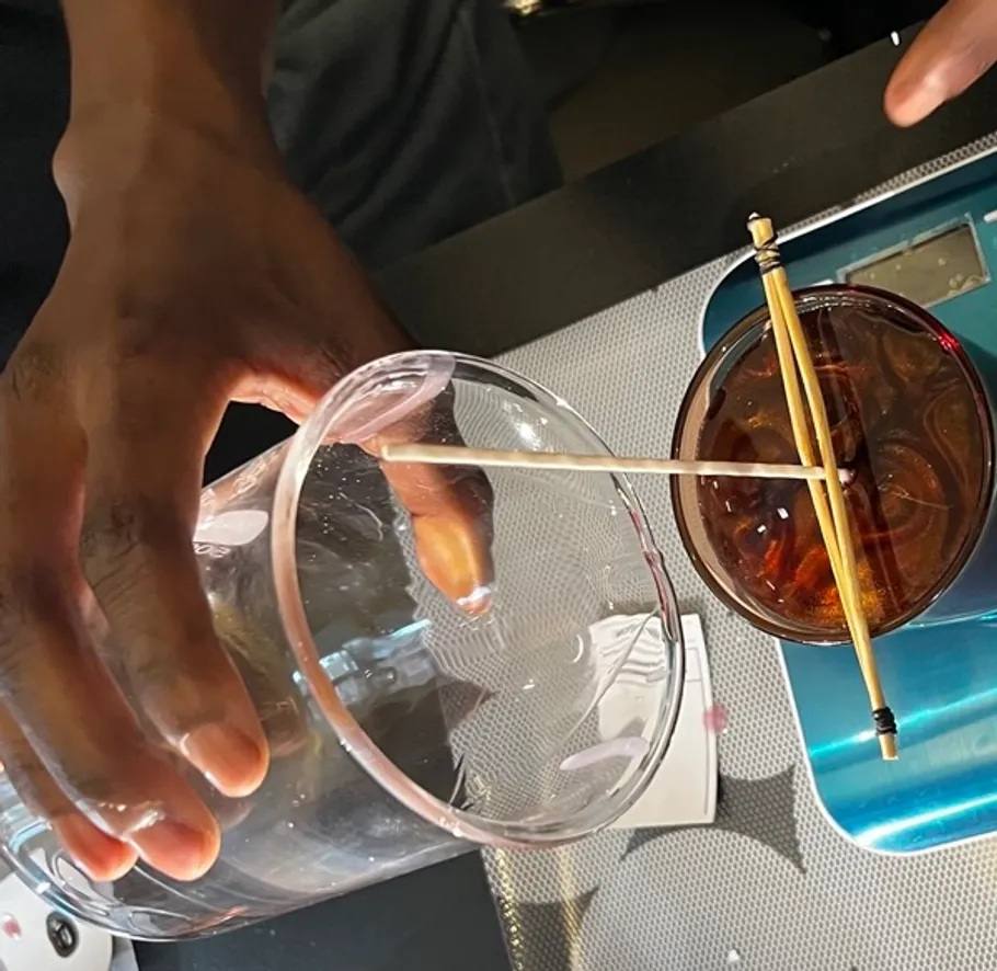 Hand balancing cup on skewers over glass.