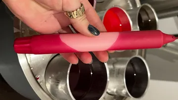 Hand holding a red unsharpened crayon over containers.