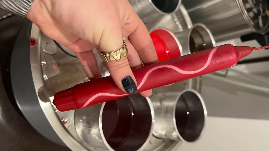 Hand hält rote Kerze, umgeben von Metallformen.