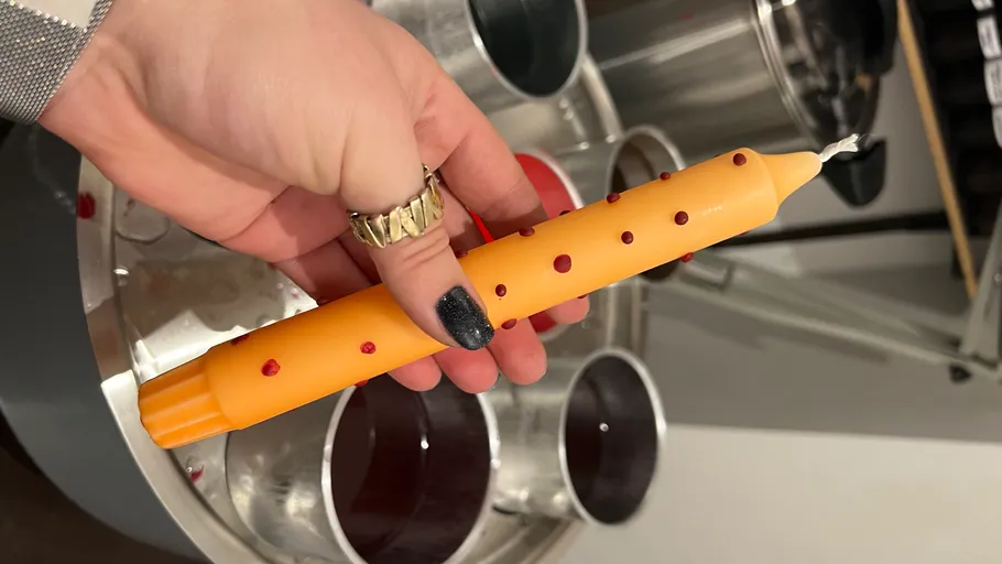 Hand hält orange Kerze mit roten Punkten.