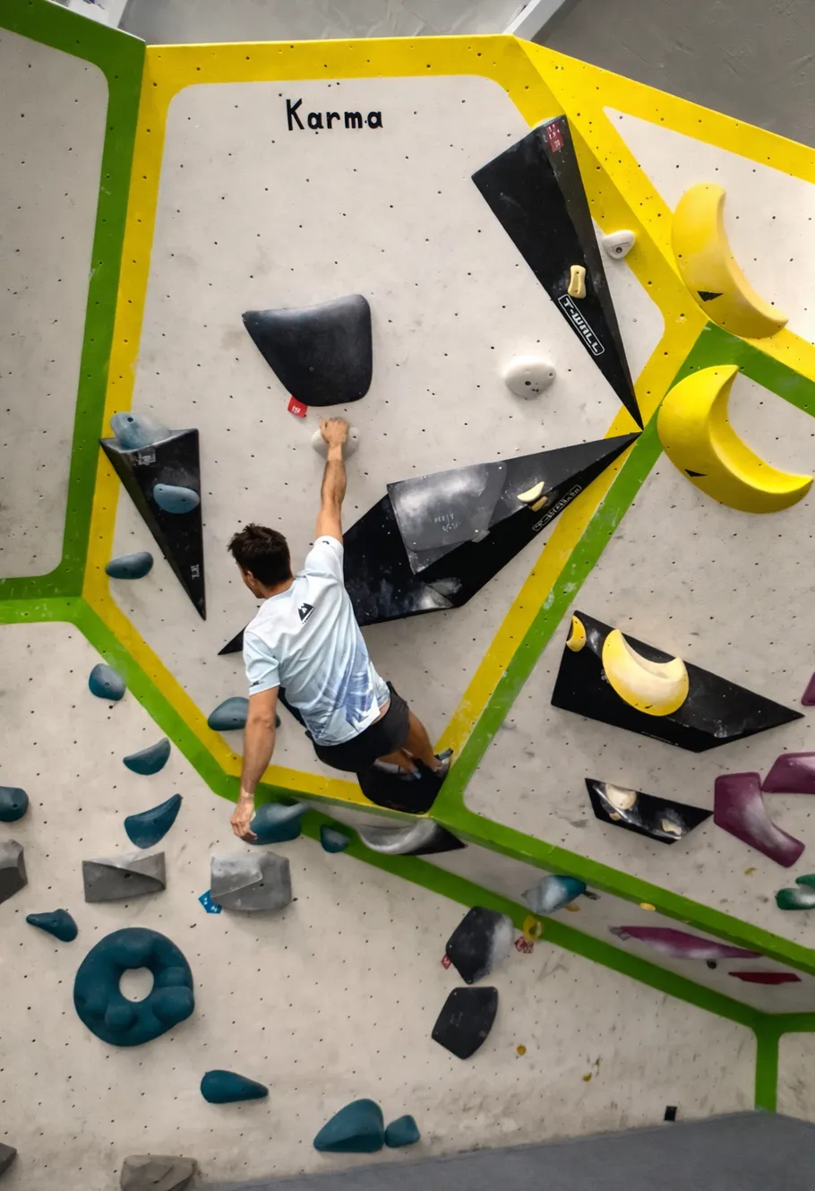 Climber ascending indoor bouldering wall with colorful holds.