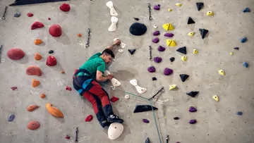 Mann klettert an bunter Hallenwand.