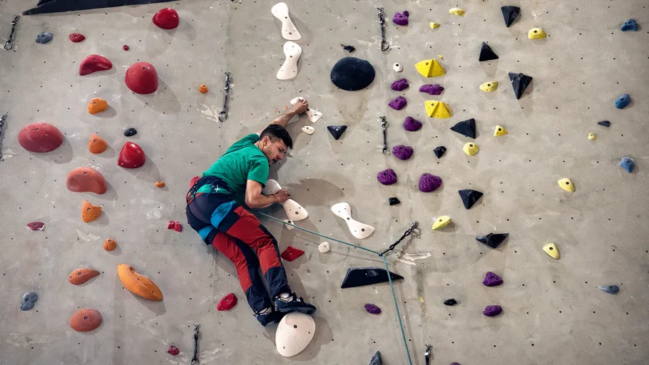 Man climbing indoor wall with colorful holds.