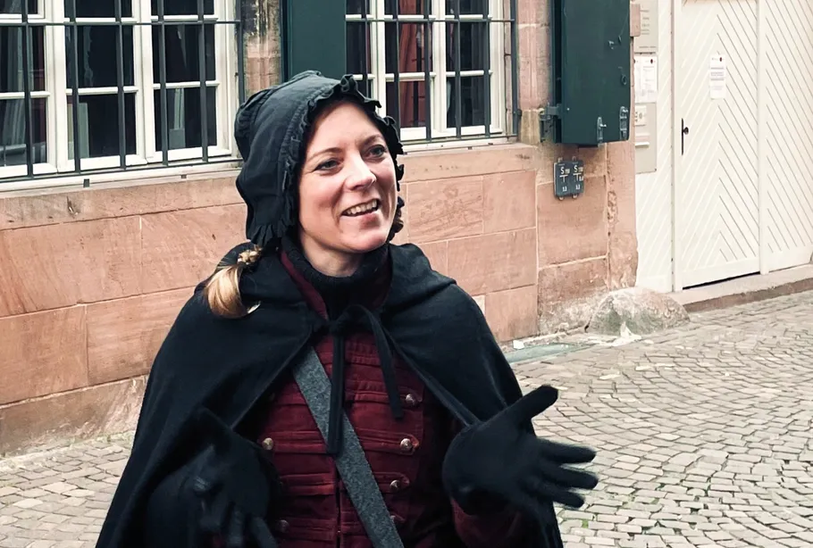 Woman in cape talking on cobblestone street.