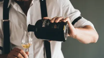 Person pouring liquor into a glass indoors.