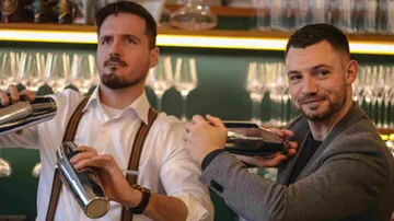 Two bartenders shaking cocktail shakers in bar.