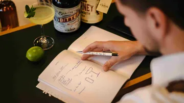 Person writing in notebook at a bar.