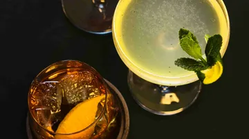 Zwei Cocktails auf einem dunklen Tisch.