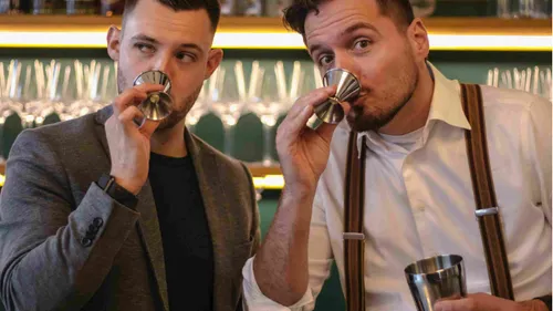 Two men smell metal jiggers in bar.